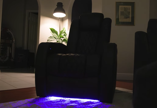 Black leather electric recliner sofa illuminated by purple LED lighting under the seat in a dark living room